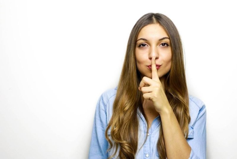 Девушка прислоняет палец к губам